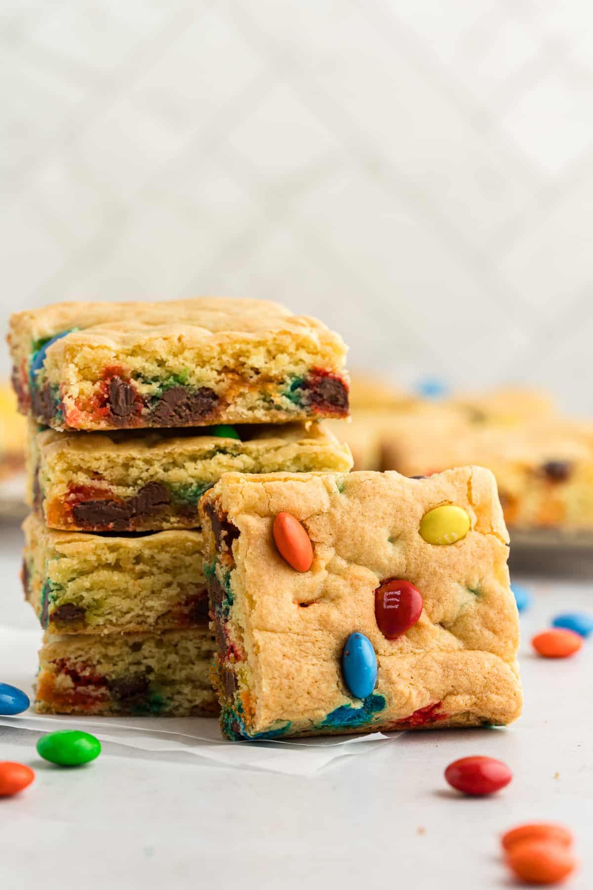 Barrette di biscotti da preparato per torte 2 a stack of cake bars with another square cake bar leaning up against the stack and more bars in the background with m&ms sprinkled around