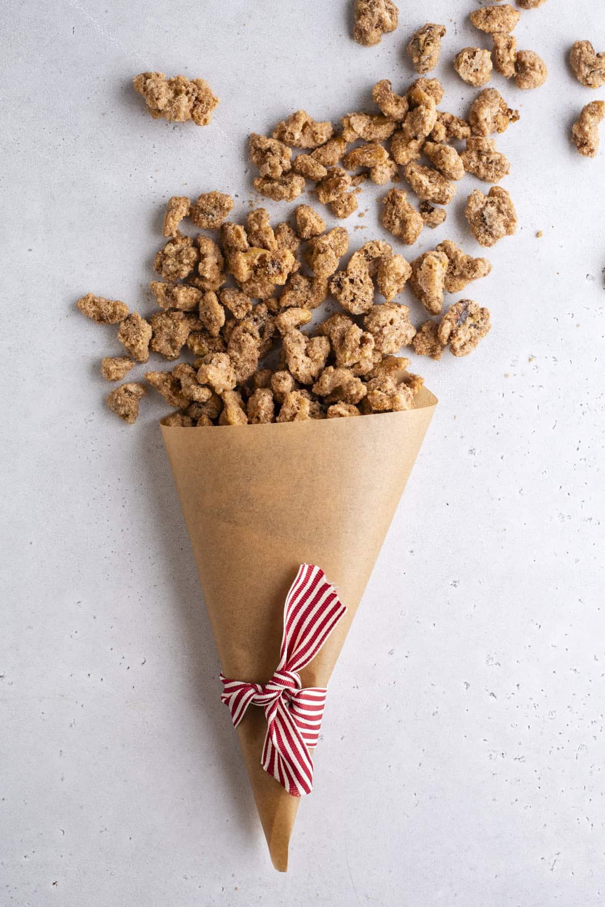 noci pralinate che fuoriescono da un cono di carta marrone con un nastro a strisce rosse e bianche annodato attorno