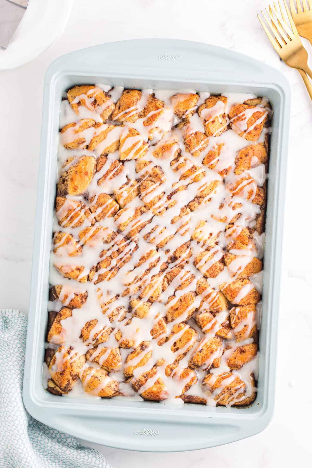 Facile Sformato di Girelle alla Cannella 2 cinnamon roll casserole with icing drizzled on top in light blue baking dish