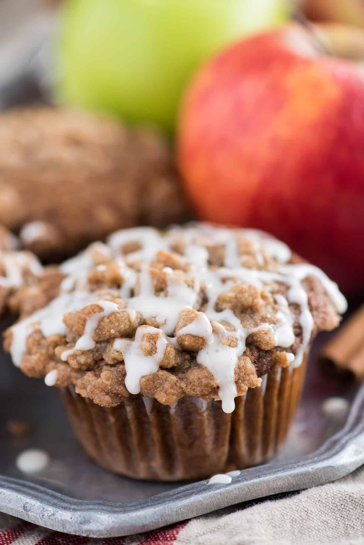Muffin speziati alla salsa di mele con crumble e glassa bianca su un piatto di metallo, con mele sullo sfondo