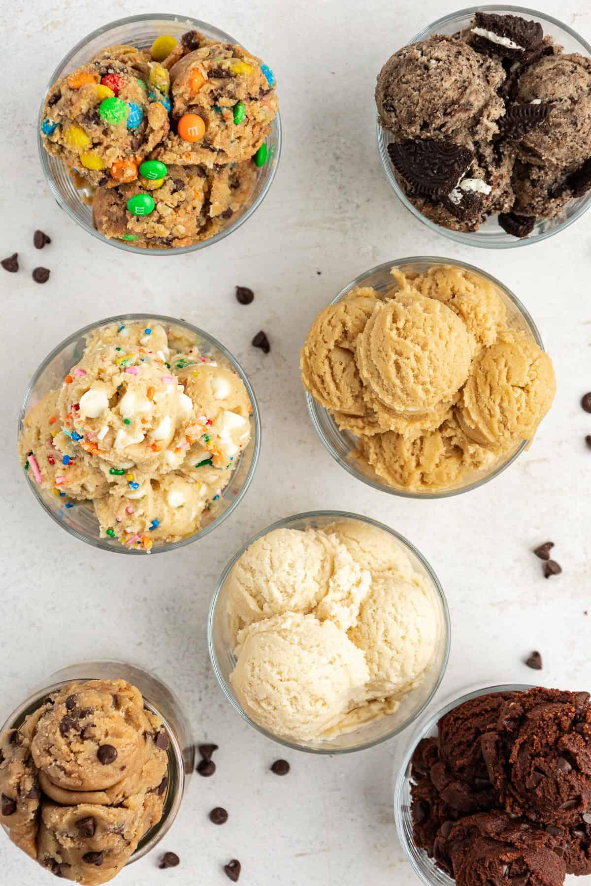 **Semplice Impasto per Biscotti Commestibile** 2 overhead view of seven clear class containers full of different cookie dough flavors including oreo, cookie monster, sugar cookie, peanut butter, funfetti, chocolate and chocolate chip