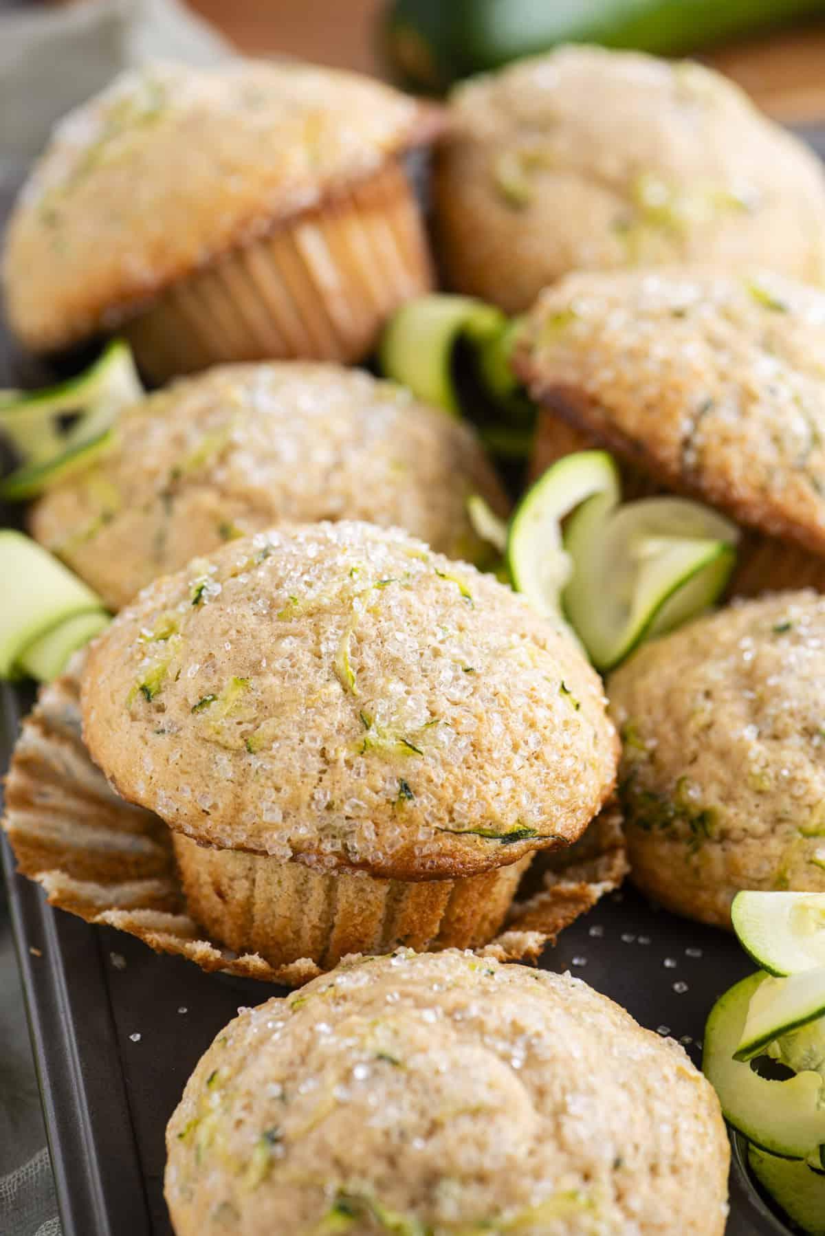 Migliori Muffin alle Zucchine 2 Muffin di zucchine impilati su una teglia da muffin, il muffin centrale nell'immagine appoggiato sul suo rivestimento sbucciato con rotoli di sottili fette di zucchine tra i muffin
