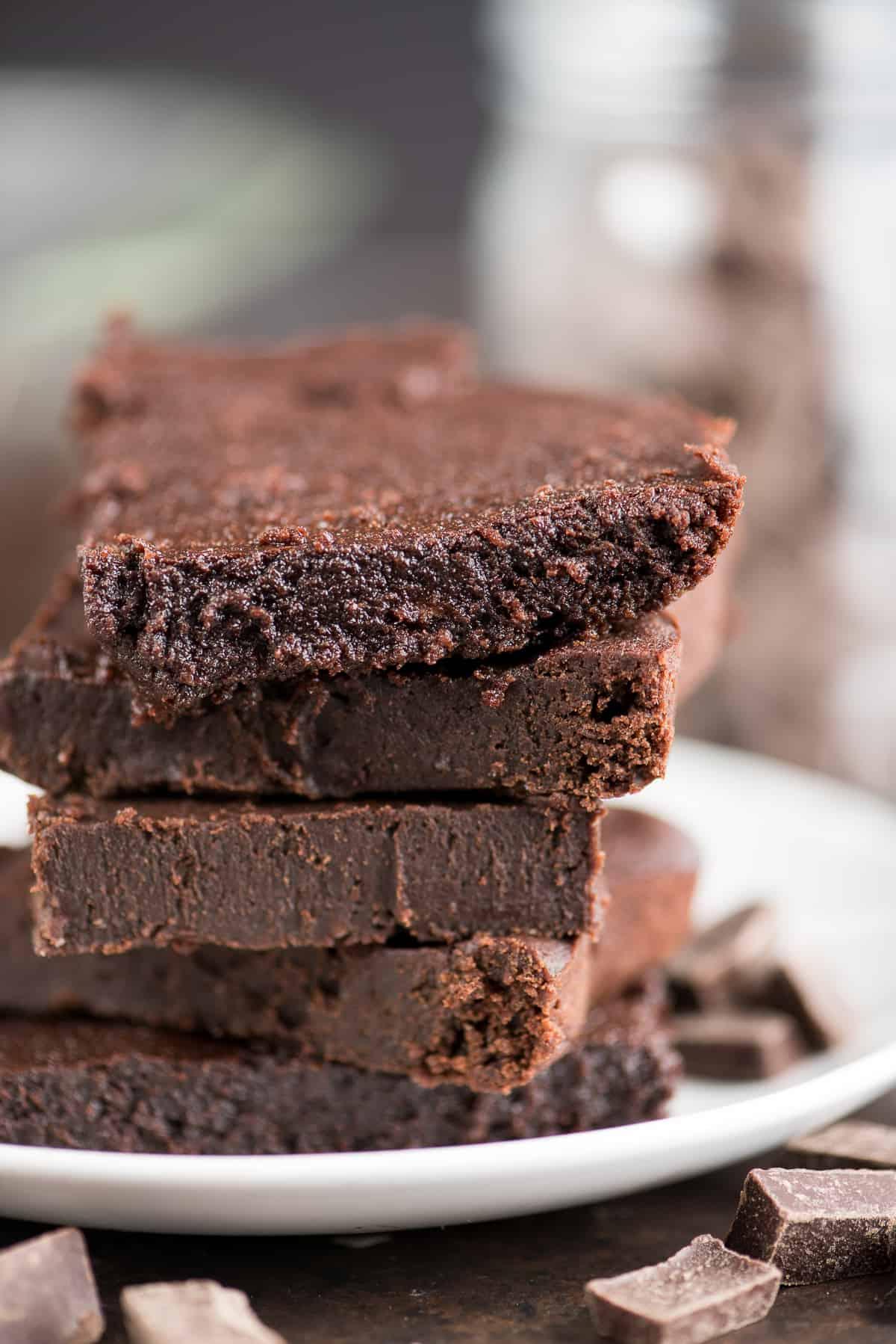 I brownies fondenti e salutari dei vostri sogni! Senza zucchero raffinato, burro o olio, con ingredienti comuni e un incredibile gusto fondente. Solo 174 calorie a fetta! Cinque brownies fondenti salutari circondati da cioccolato su un piatto bianco.