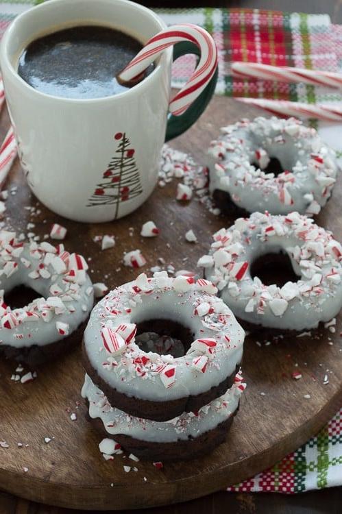Ciambelle al cioccolato cotte al forno, aromatizzate alla menta piperita, guarnite con cioccolato bianco e bastoncini di zucchero tritati.