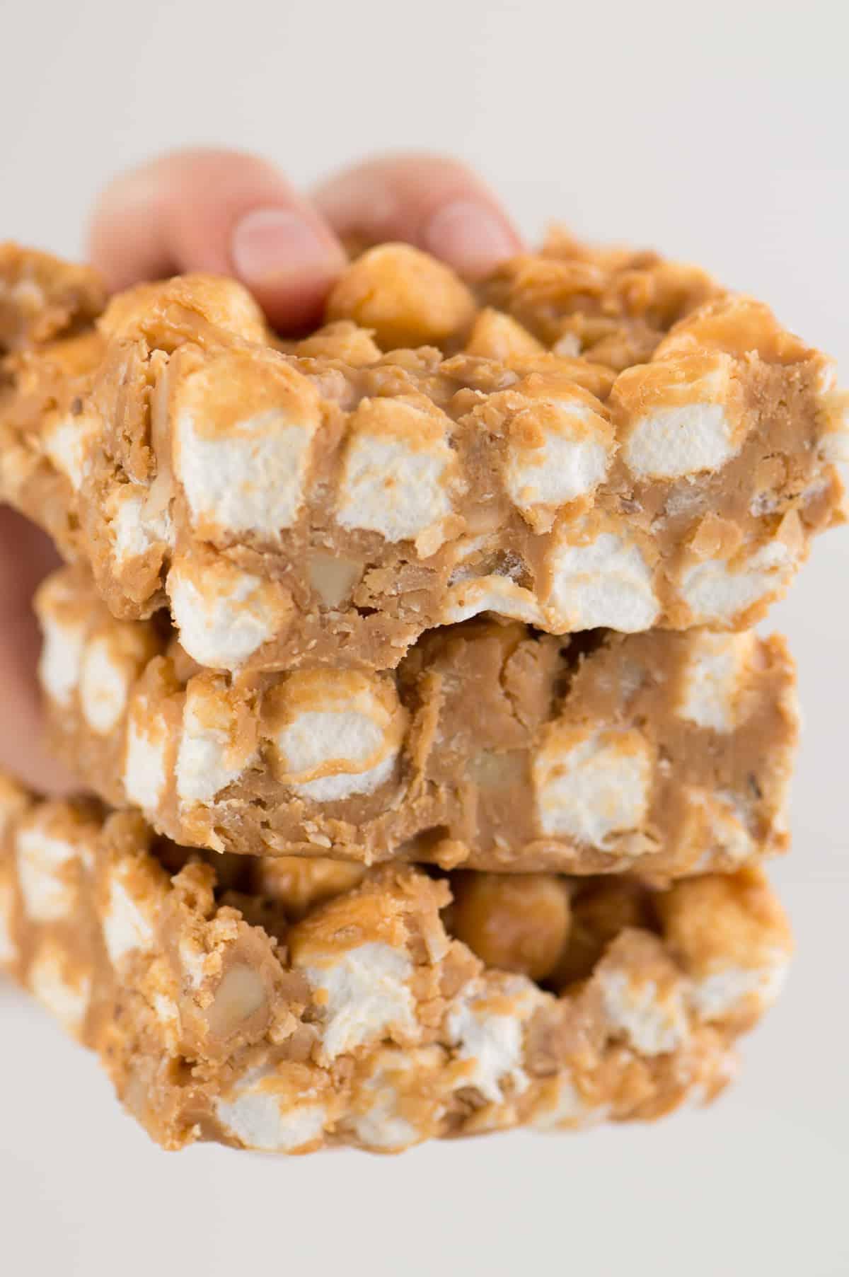 Barrette Senza Cottura al Butterscotch e Marshmallow 2 Mano che tiene 3 barrette marshmallow al butterscotch su sfondo bianco, mostrando la loro consistenza morbida e la copertura lucida.