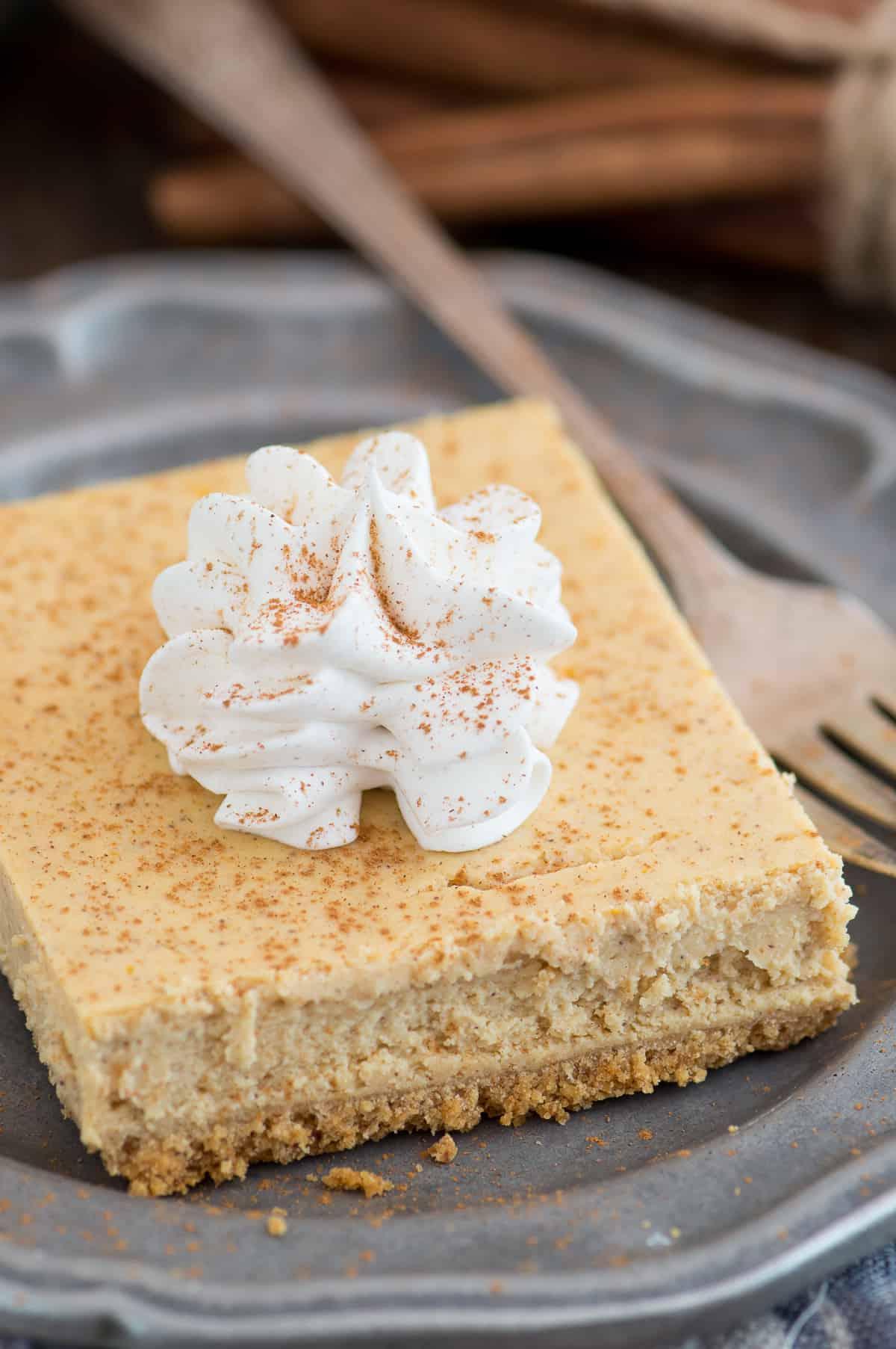 Barrette di Cheesecake alla Zucca 2 Fetta di barretta di cheesecake alla zucca con una cucchiaiata di panna montata su un piatto di metallo