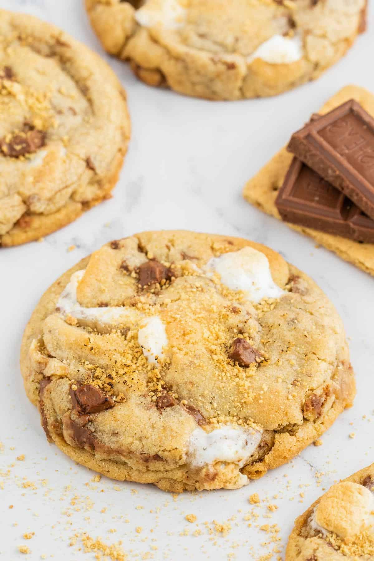 Ricetta Biscotti S'mores con Graham Crackers 2 biscotti s'mores disposti vicino a un cracker Graham con pezzi di barretta Hershey sopra