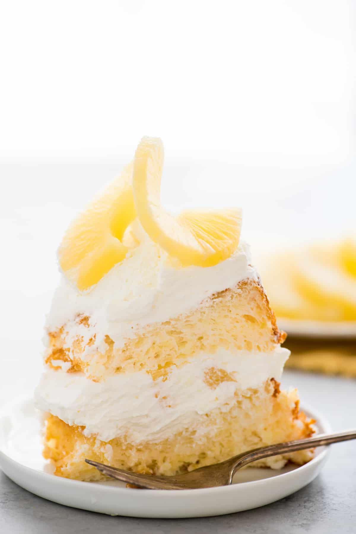 Fetta di torta Angel Food all'ananas con panna montata e ananas su piatto bianco su sfondo bianco