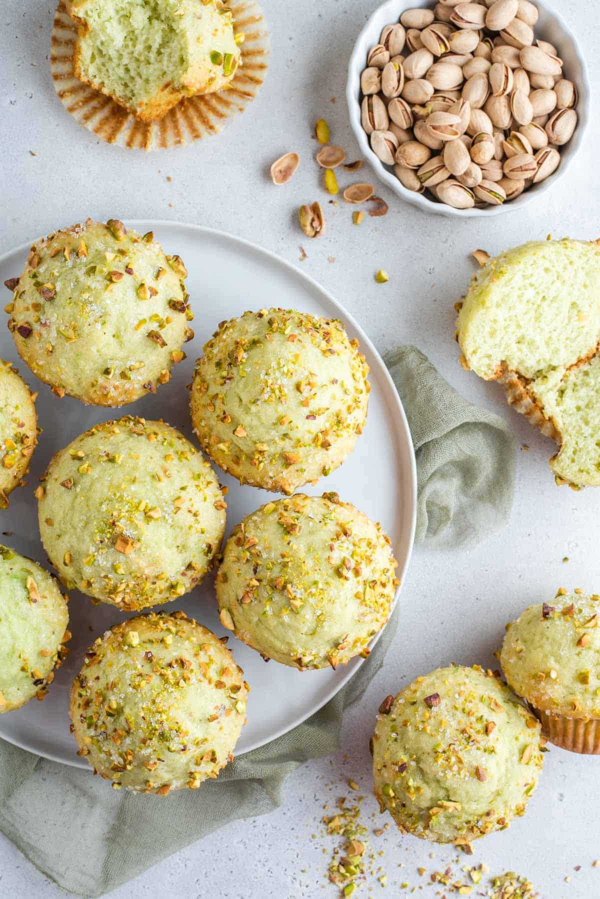 Muffin al Pistacchio 2 Pistachio muffins on a plate, with one cut in half, and a bowl of whole pistachios next to them.