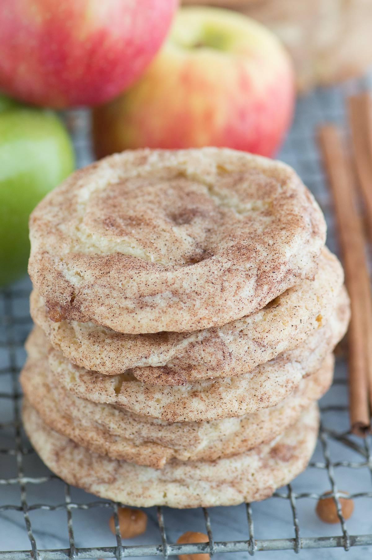 Snickerdoodles al Caramello e Mela 2 Biscotti snickerdoodle alle mele caramellate impilati su una griglia di raffreddamento metallica con mele sullo sfondo