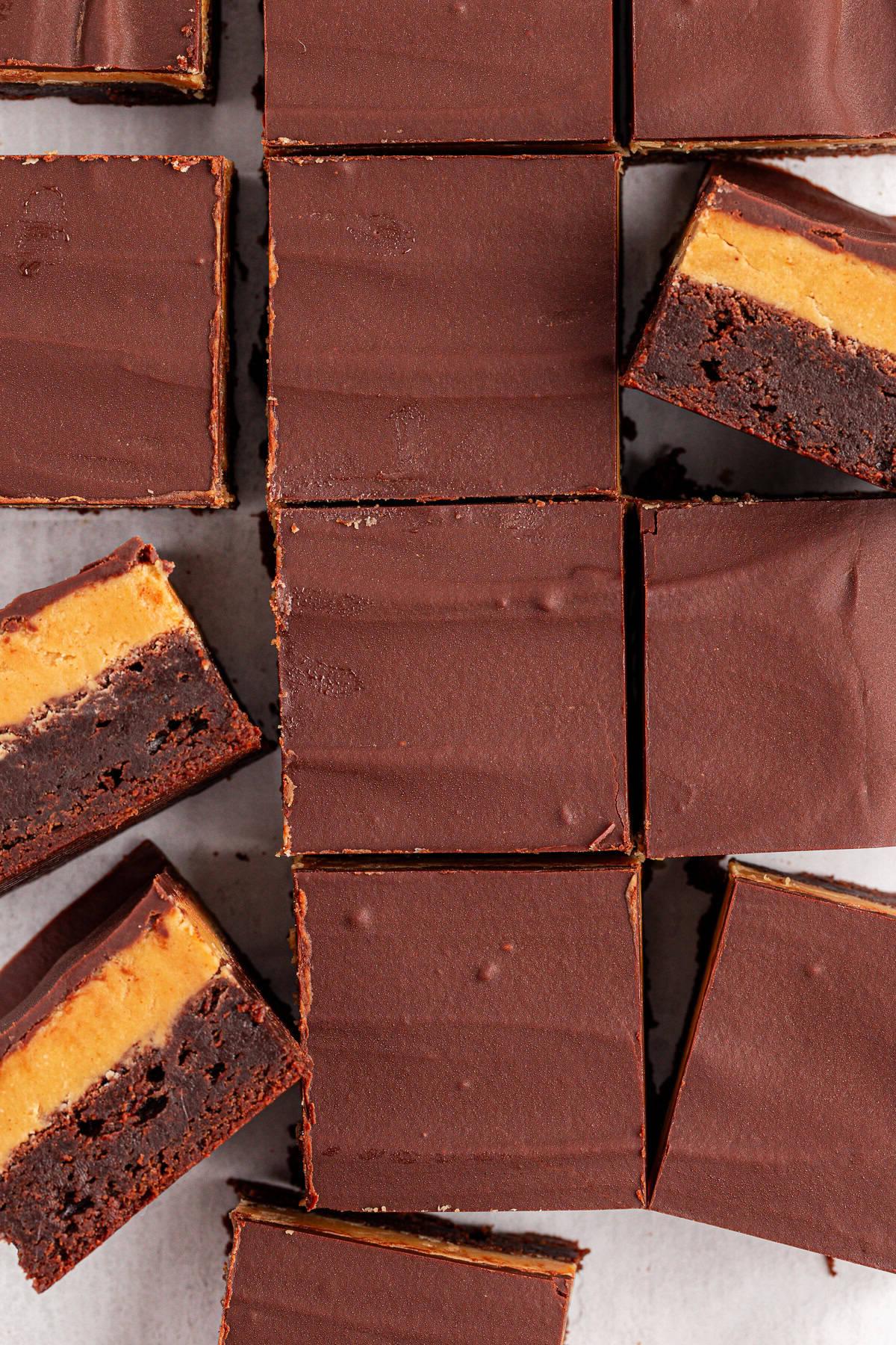 Brownies Buckeye a tre strati: una spessa e lucida copertura di cioccolato, uno strato centrale al burro d'arachidi e una base scura di brownie. Alcune barrette sono impilate per mostrare i distinti strati e le ricche consistenze.