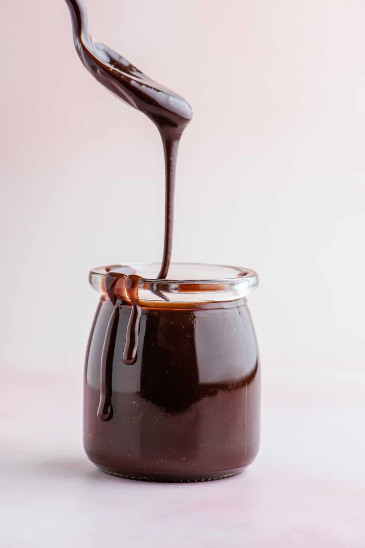 **Salsa Calda al Cioccolato Fondente** 2 Salsa al cioccolato calda in un barattolo di vetro con un cucchiaio che mostra la salsa densa e calda che gocciola nel barattolo