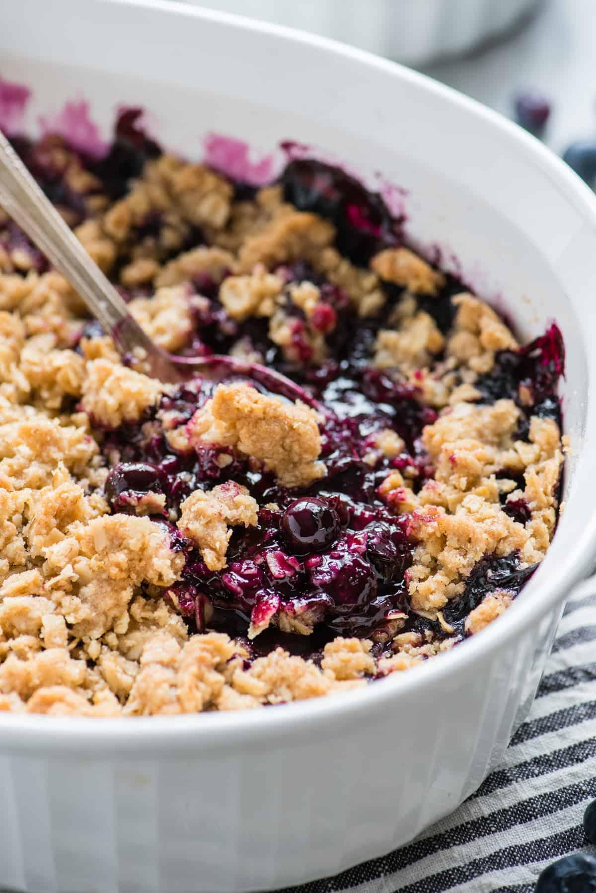 Crumble di Mirtilli Freschi 2 Crumble ai mirtilli in una teglia bianca con un cucchiaio di metallo