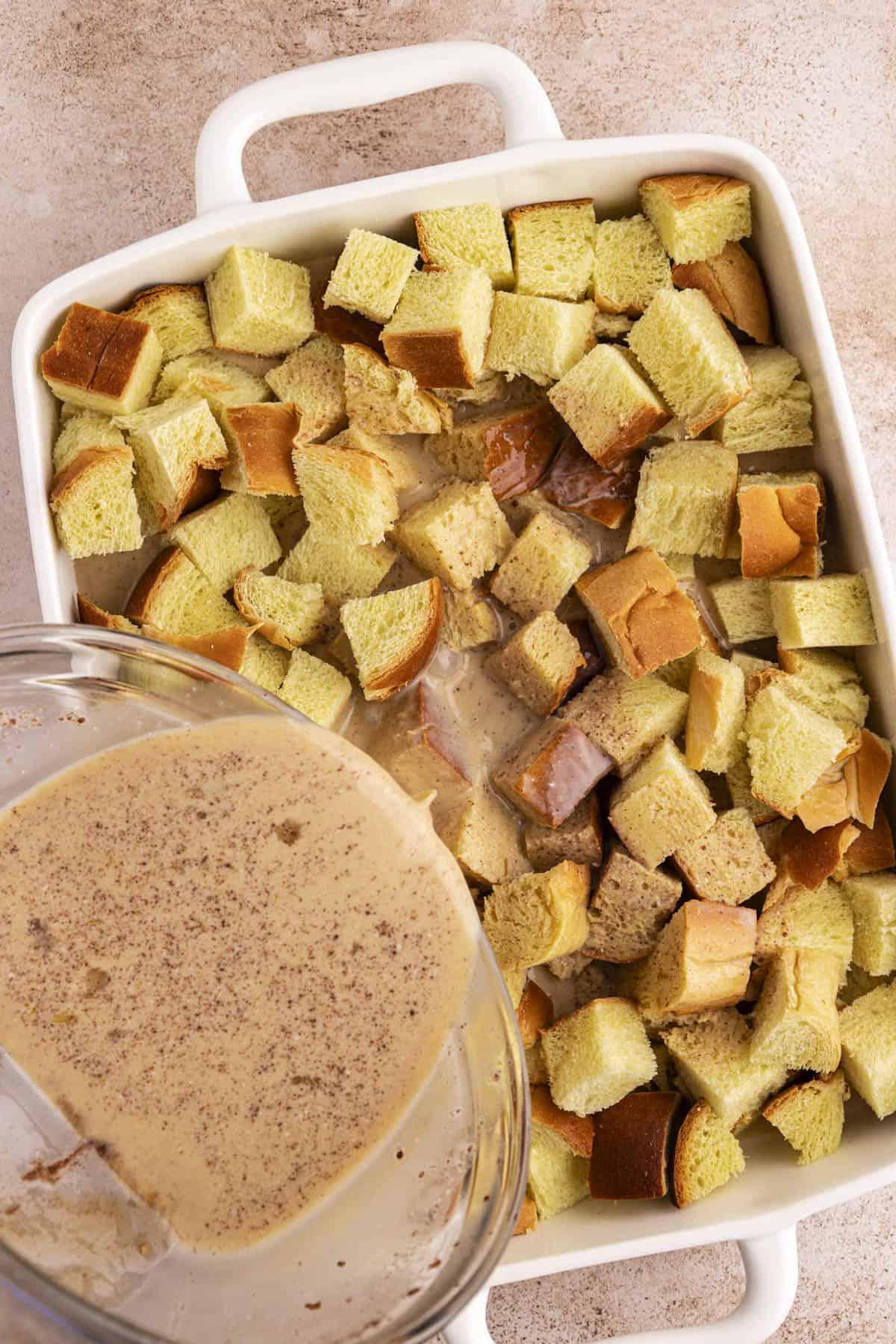 Migliore Ricetta per Budino di French Toast 11 Una teglia bianca piena di cubetti di pane con una miscela liquida versata sopra.