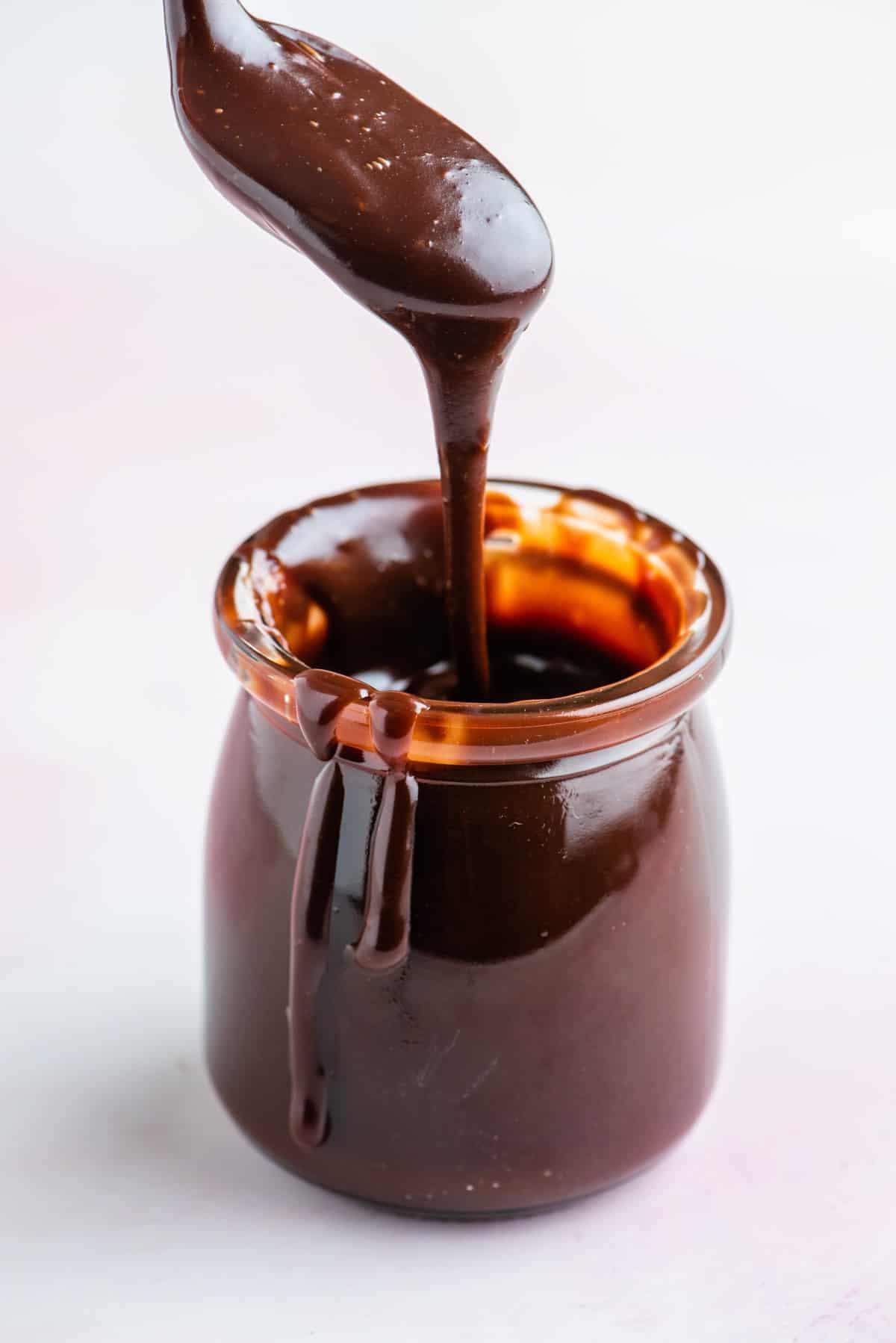 **Salsa Calda al Cioccolato Fondente** 12 Un barattolo di salsa hot fudge con un cucchiaio sopra pieno di salsa che gocciola e salsa che gocciola lungo il lato del barattolo