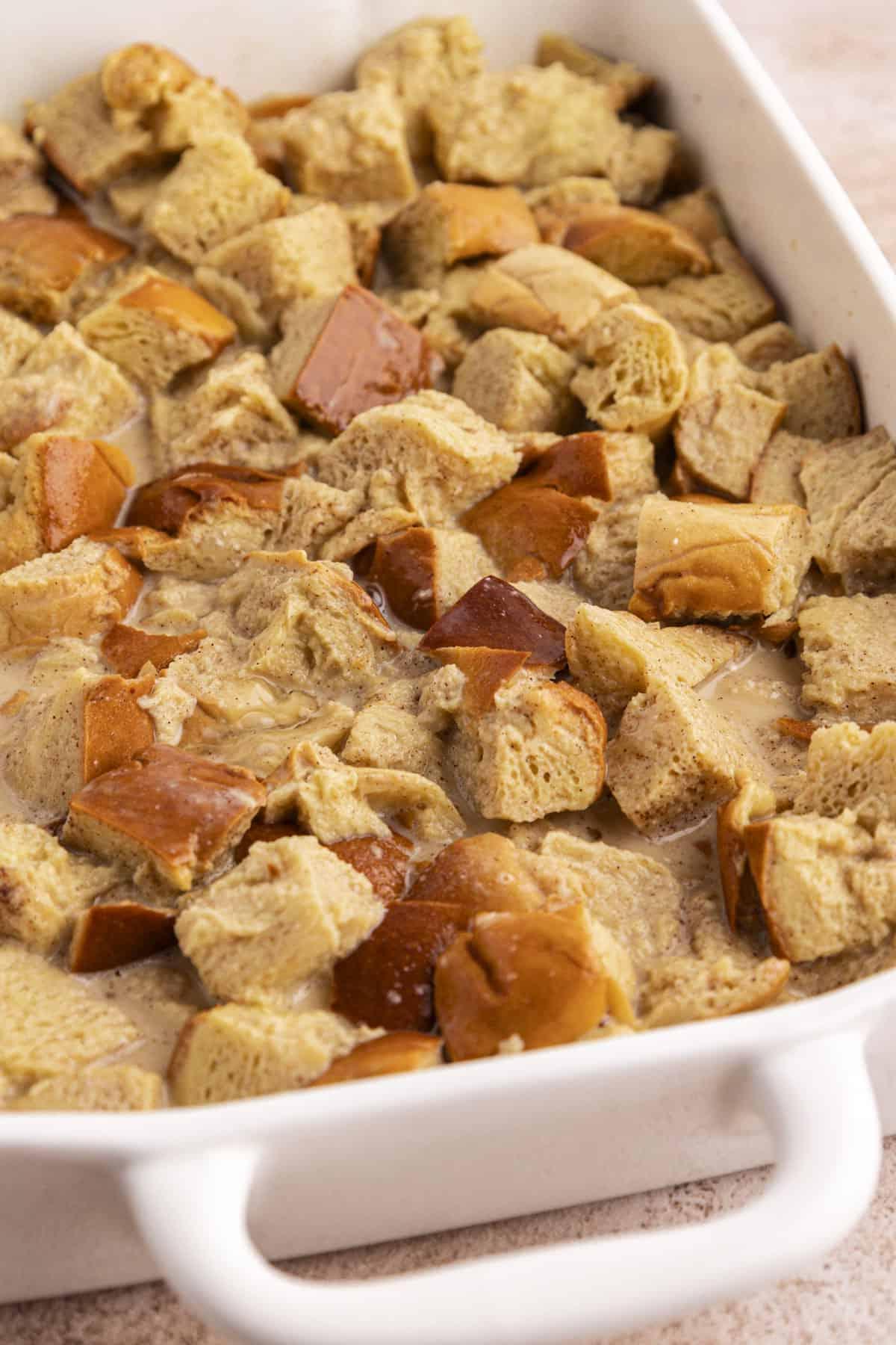 Migliore Ricetta per Budino di French Toast 12 Cubetti di pane imbevuti in una miscela liquida in una teglia bianca.