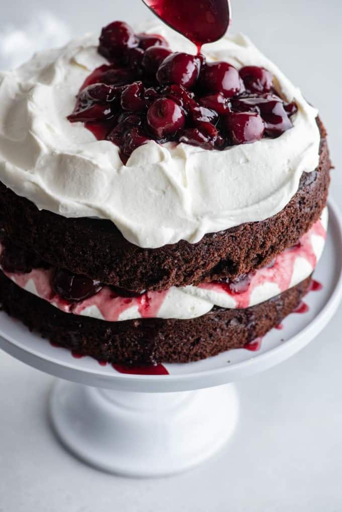 Torta Foresta Nera 12 Torta Foresta Nera su un'alzatina bianca con uno strato di torta al cioccolato, panna montata, ciliegie, più torta al cioccolato, più panna montata e ciliegie aggiunte sopra