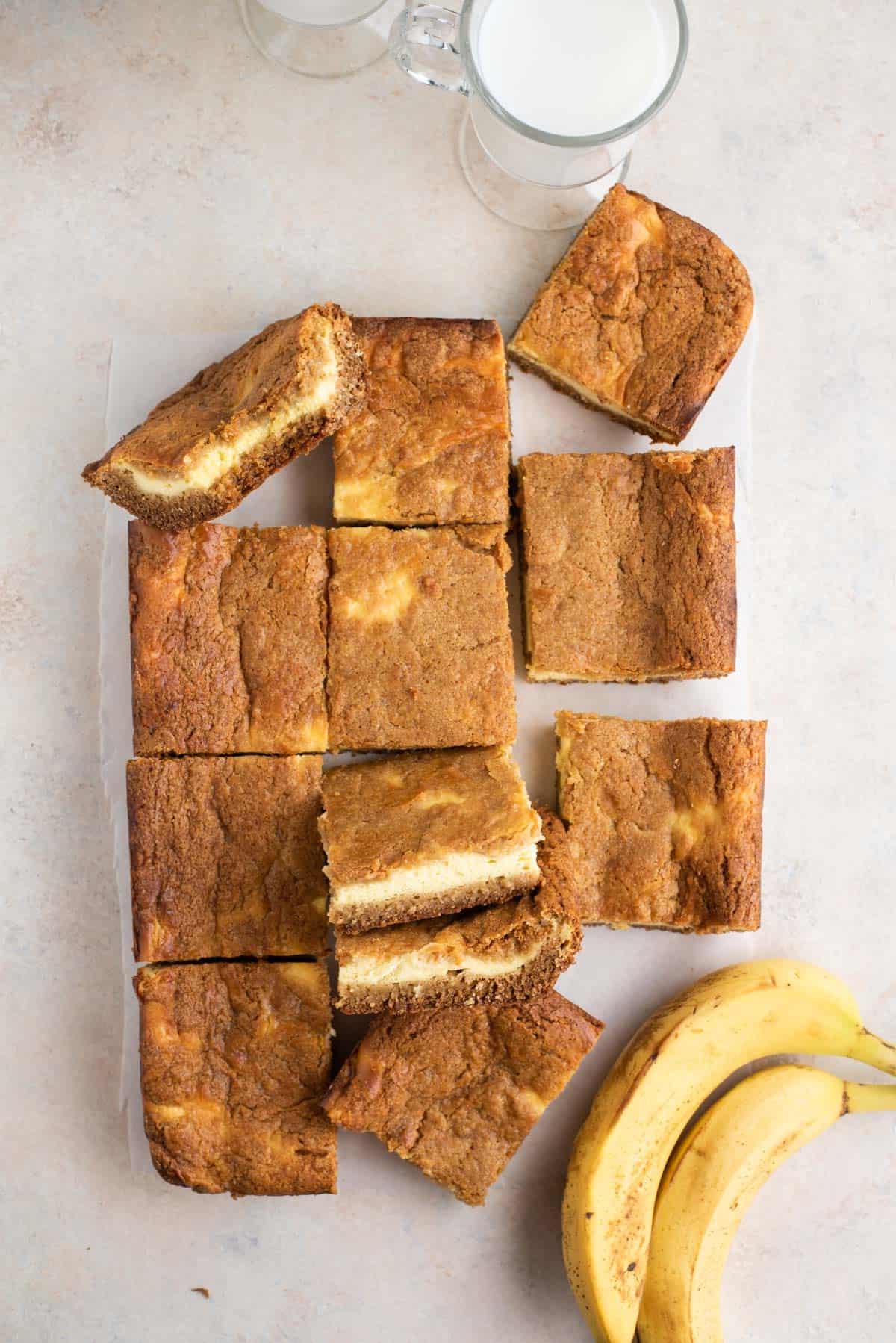 Brownies al Budino di Banana 12 Brownies al budino di banana disposti su un bancone con banane e una tazza di latte