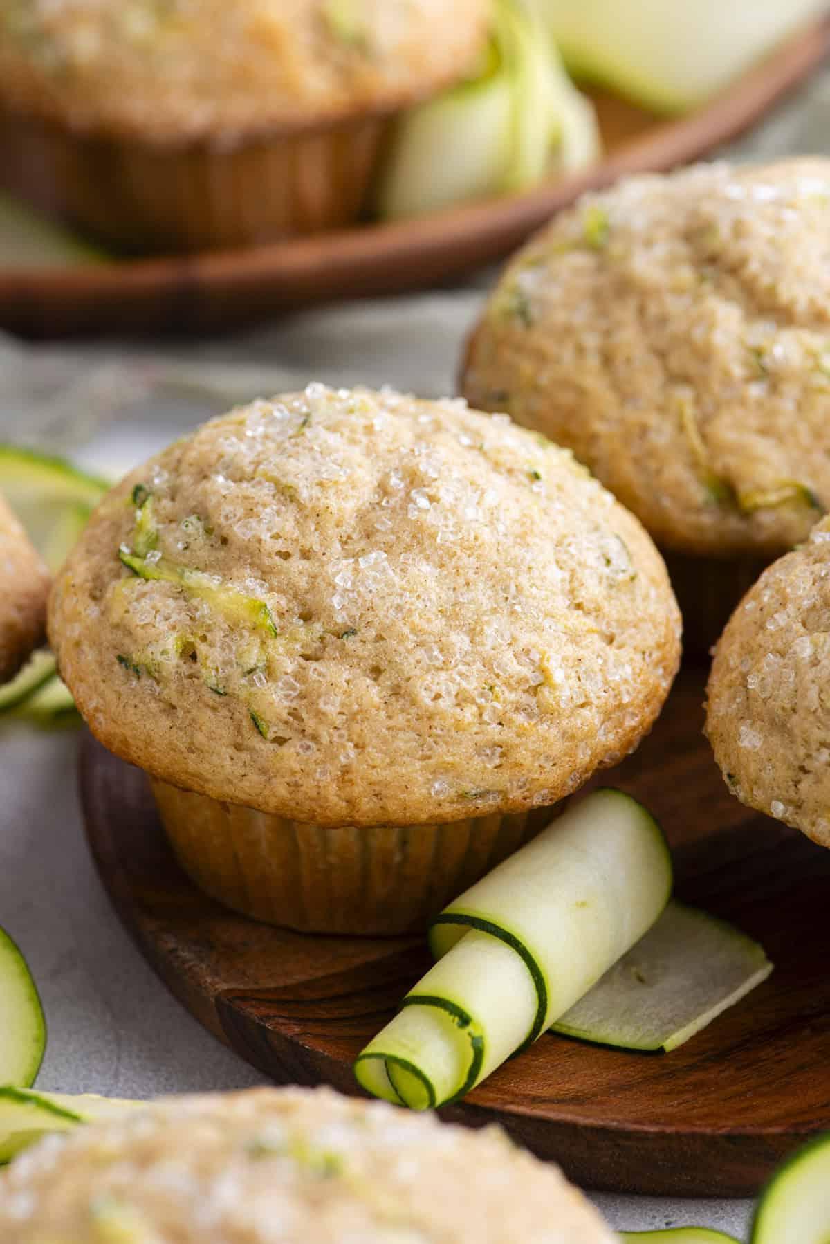 Migliori Muffin alle Zucchine 12 Muffin di zucchine su un piatto di legno con altri muffin e sottili fette di zucchine sparse intorno