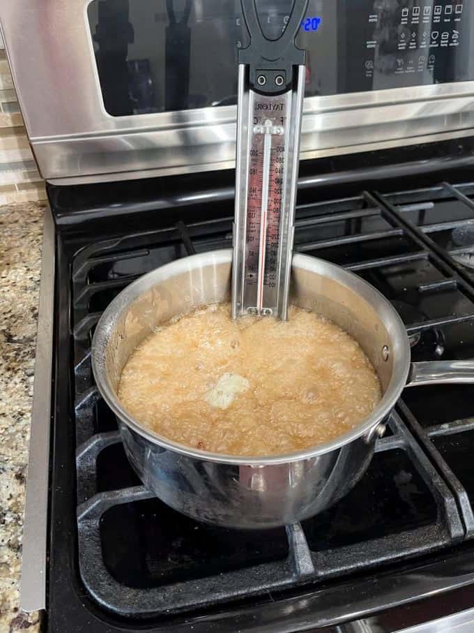 Il miglior croccante di arachidi 12 Una pentola sul fornello con zucchero semolato, acqua, sciroppo di mais, bicarbonato di sodio, estratto di vaniglia e arachidi che cuociono e un termometro per dolci attaccato al lato