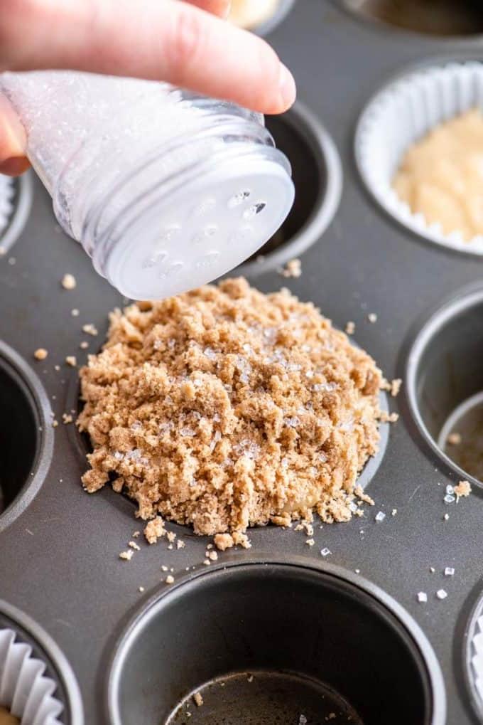 Muffin alla Sbriciolata 13 mano che aggiunge zucchero bianco granulato sulla parte superiore del muffin