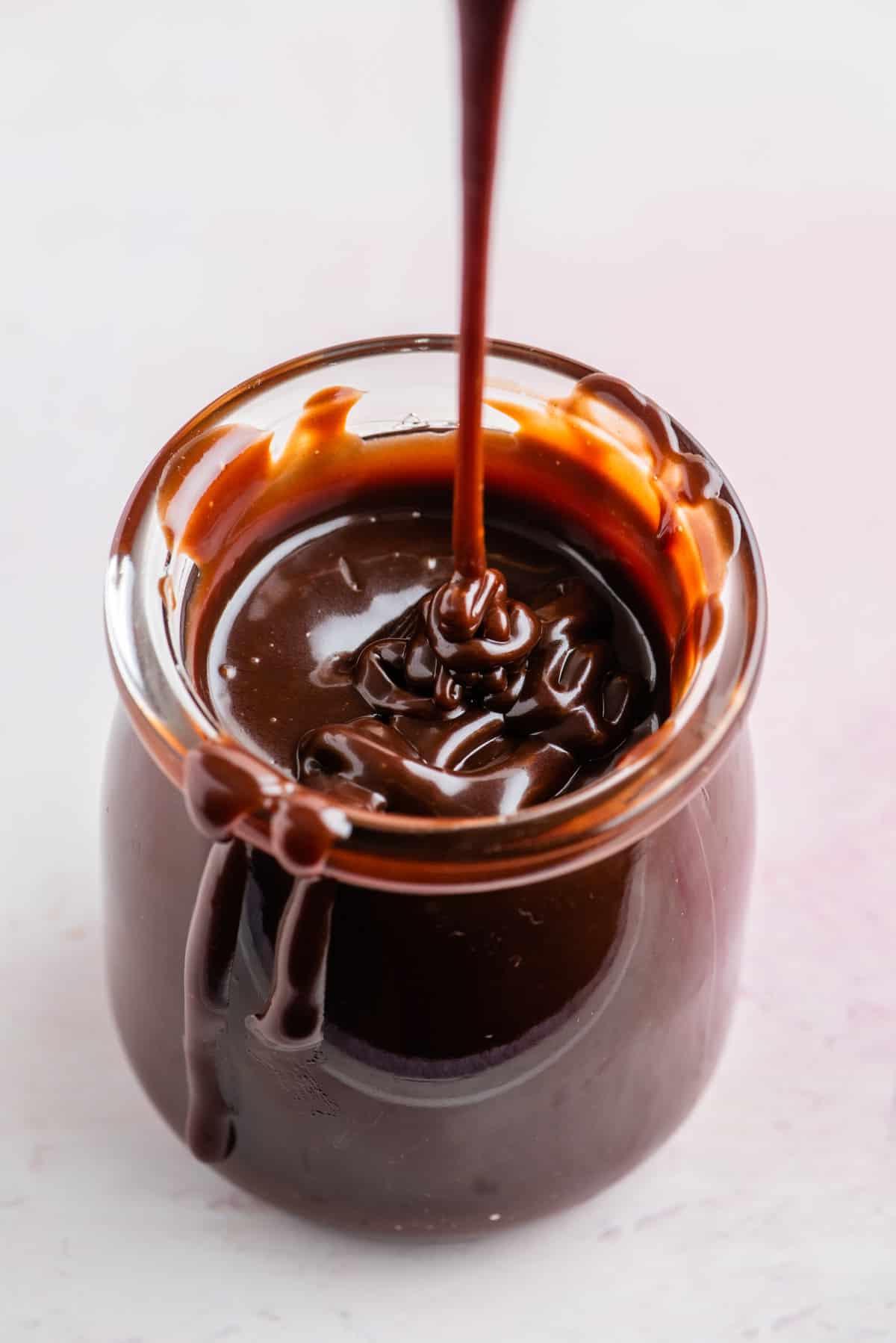 **Salsa Calda al Cioccolato Fondente** 13 Un barattolo di salsa hot fudge con un filo di salsa che gocciola e salsa che gocciola lungo il lato del barattolo