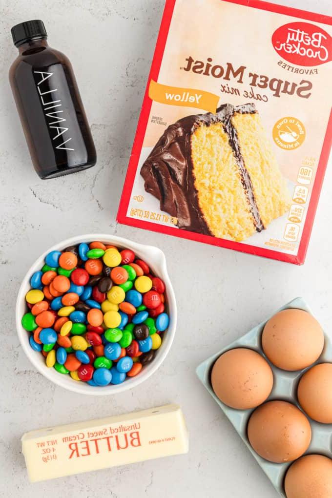 Barrette di biscotti da preparato per torte 13 a box of cake mix, a bottle of vanilla extract, a bowl of M&Ms, a crate of eggs, and a stick of butter