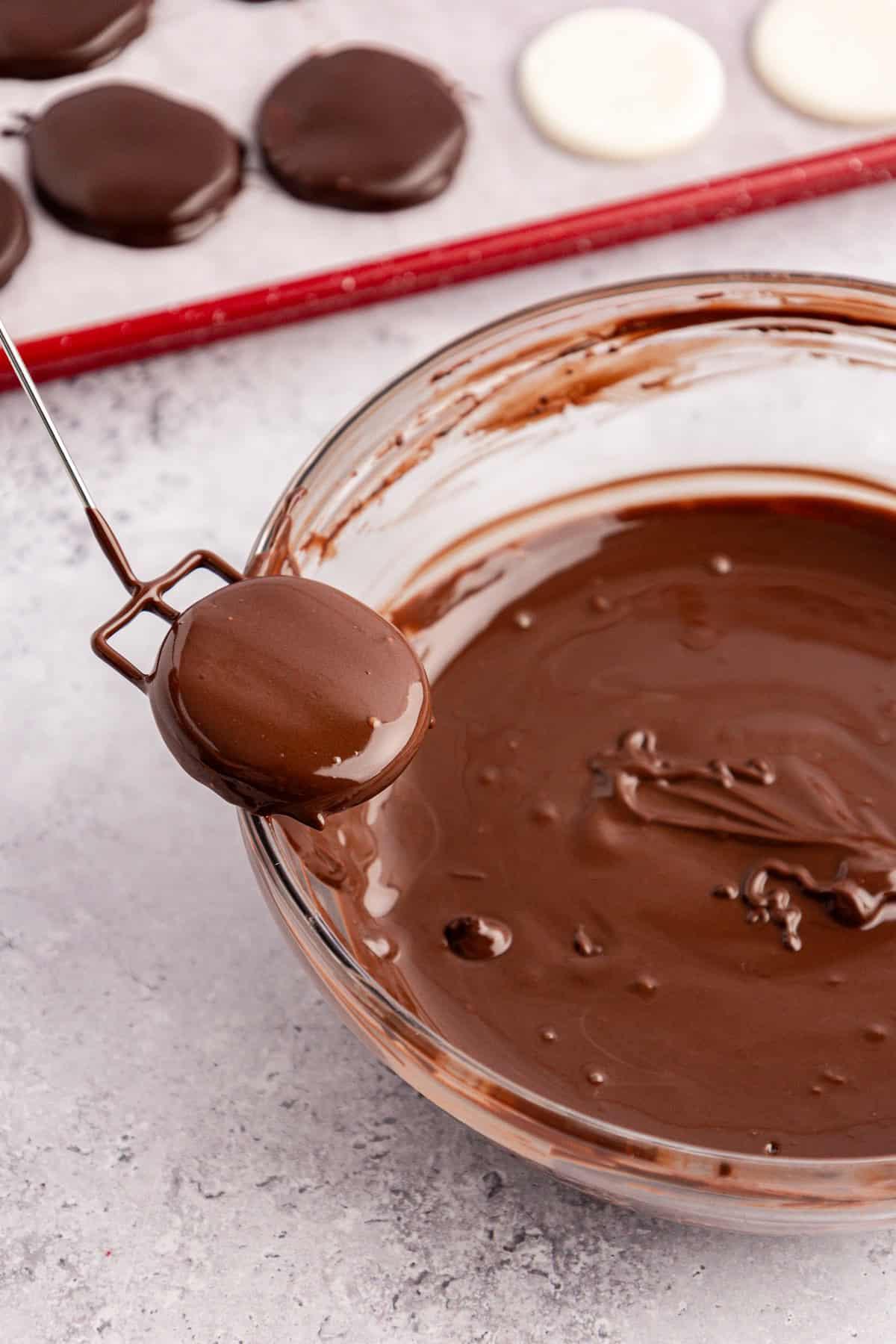 Dischetti alla menta piperita York fatti in casa 13 Un patty alla menta appena immerso in una ciotola di vetro trasparente di cioccolato fuso viene sollevato dal bordo della ciotola