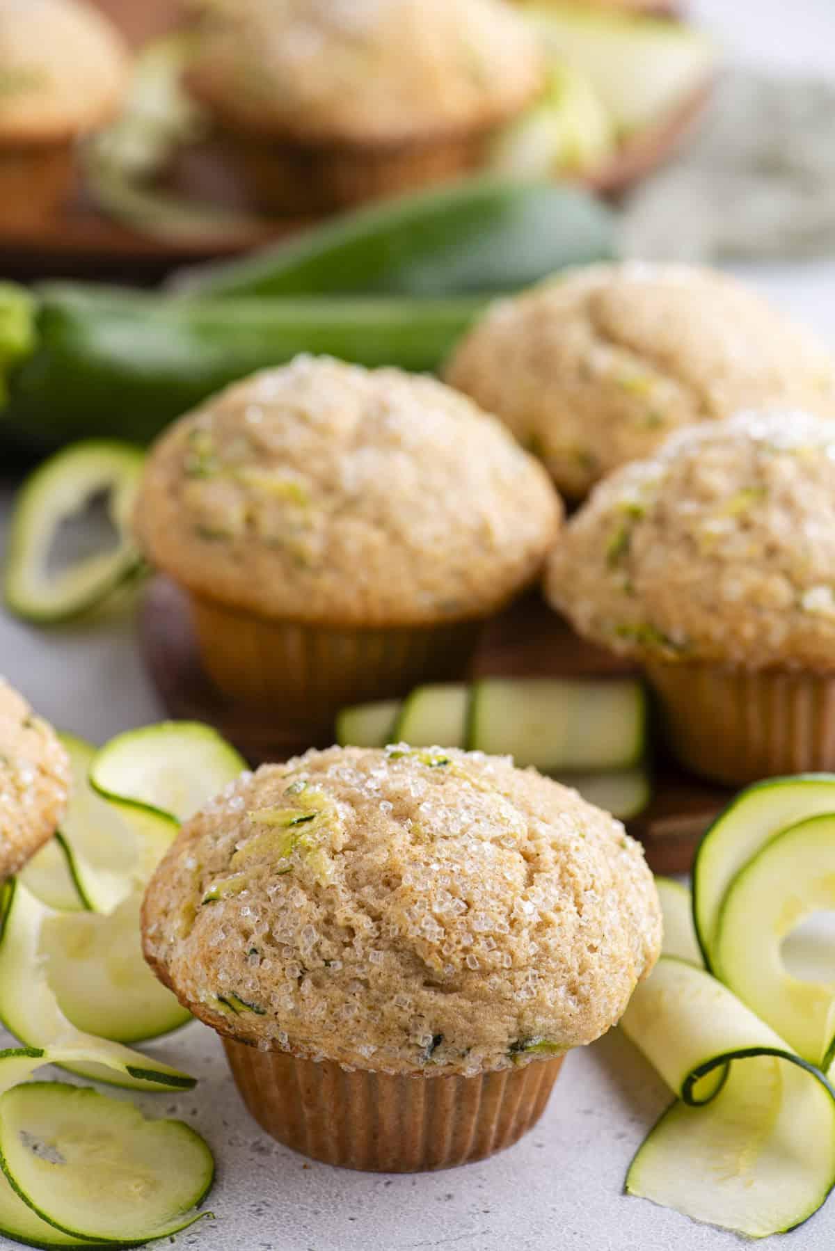 Migliori Muffin alle Zucchine 13 Un muffin di zucchine con fette di zucchine intorno e altri muffin e zucchine intere sullo sfondo