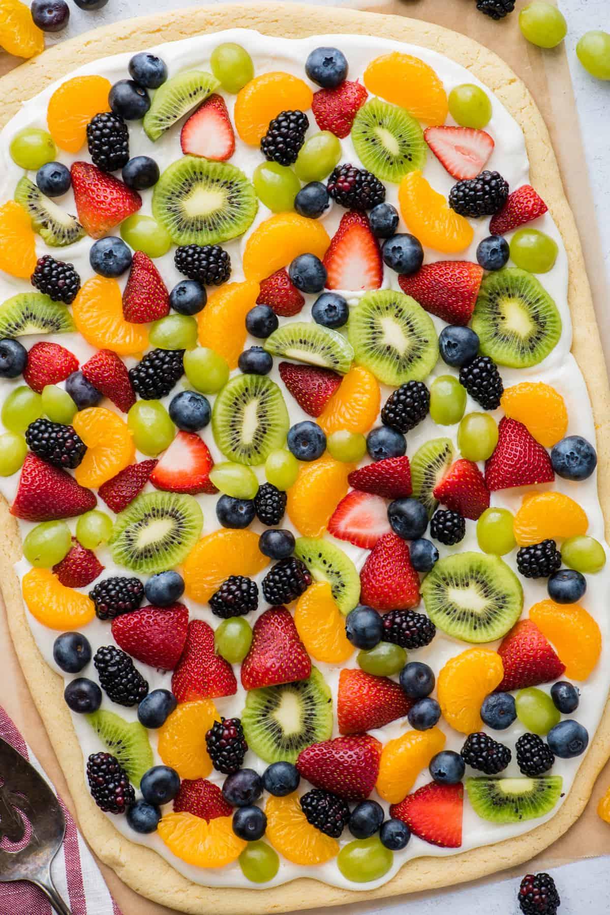 Una pizza di frutta intera con fragole, mirtilli, mandarini, kiwi e uva su carta da forno marrone