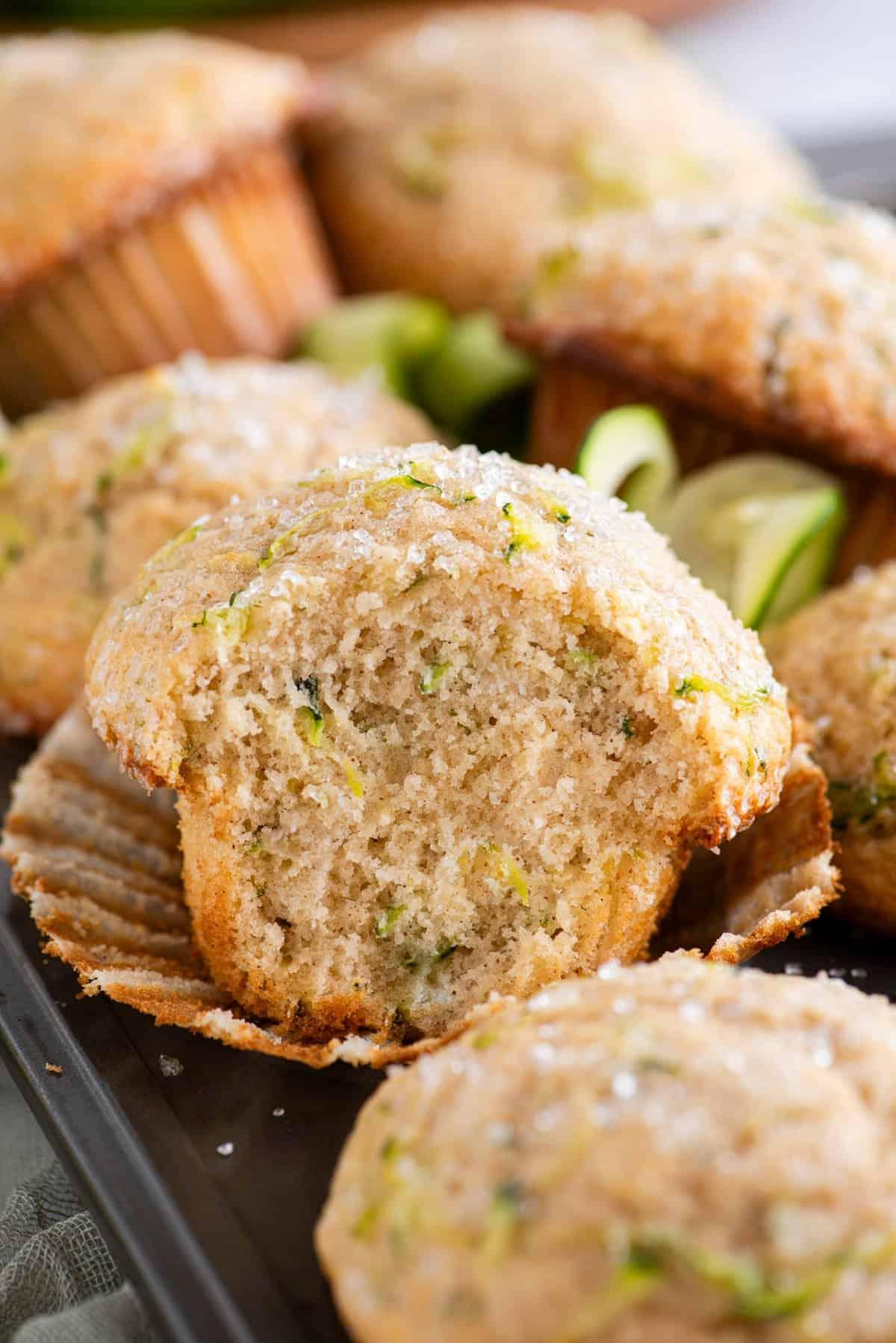Migliori Muffin alle Zucchine 14 Muffin di zucchine impilati su una teglia per muffin con quello al centro dell'immagine sbucciato dal suo pirottino e un morso mancante