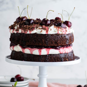 Torta Foresta Nera 14 Torta Foresta Nera su un'alzatina bianca con pile di piatti bianchi e ciliegie che la circondano