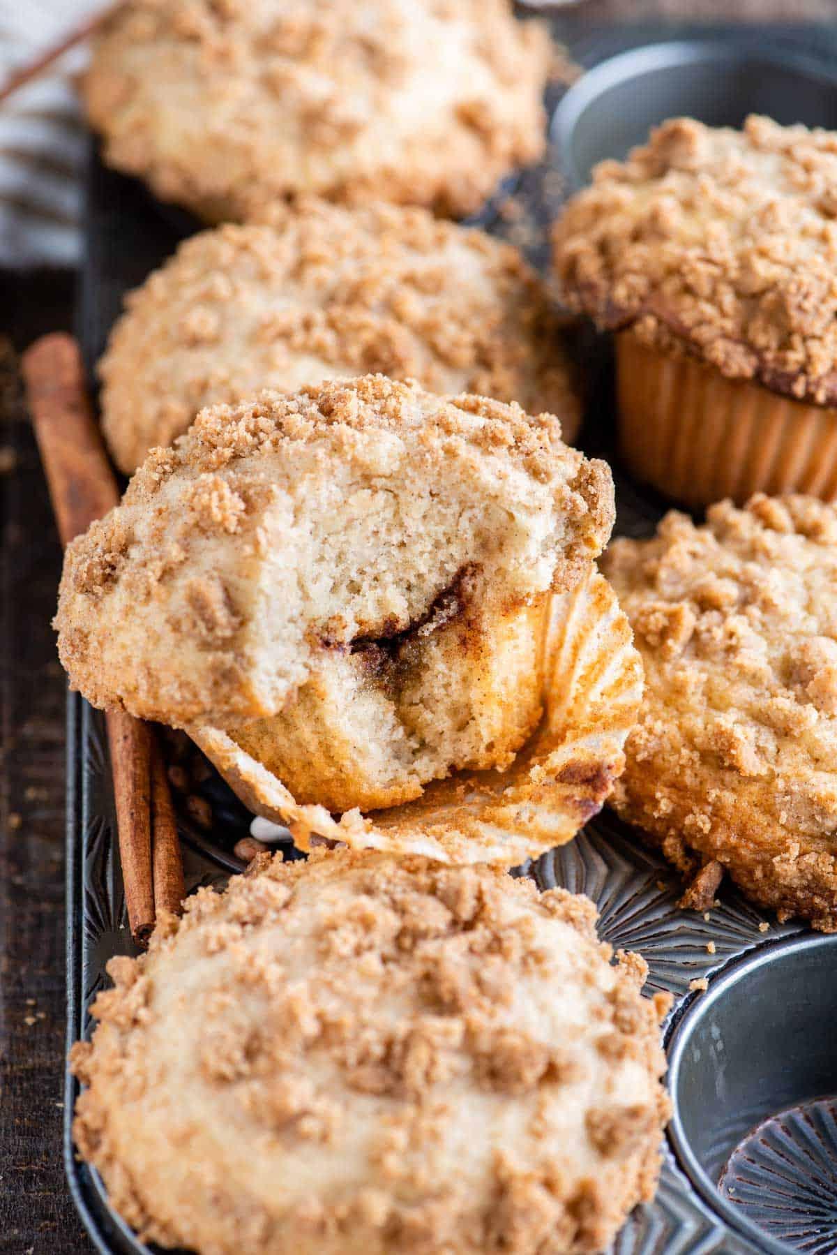 Muffin alla Sbriciolata 14 muffin al caffè con un morso che mostra lo strato di cannella all'interno nella teglia da muffin metallica