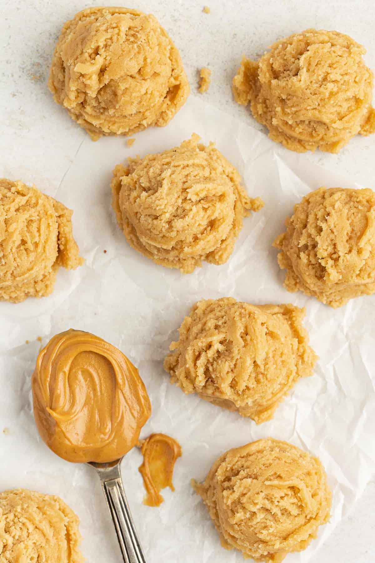 **Semplice Impasto per Biscotti Commestibile** 16 edible peanut butter cookie dough balls on white parchment paper with one spoon full of peanut butter