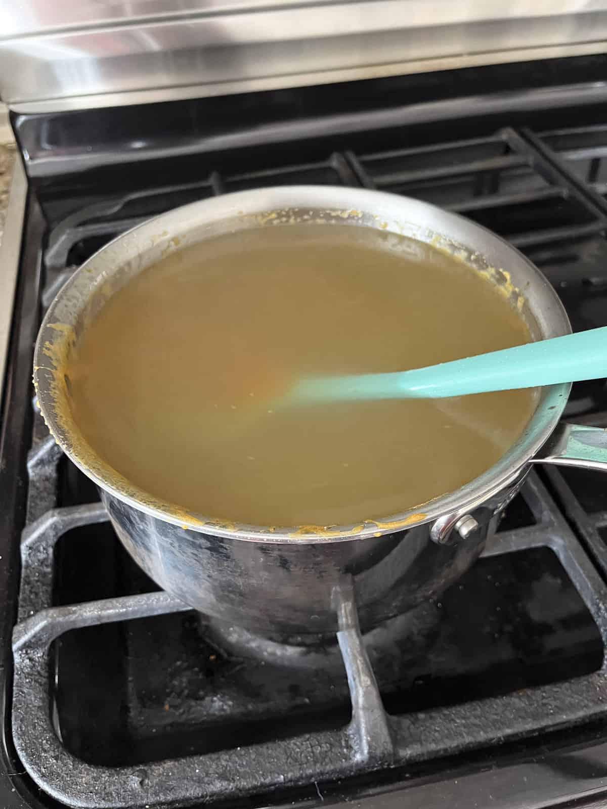 Il miglior croccante di arachidi 16 Una pentola sul fornello piena d'acqua e residui di dolci avanzati dalla preparazione del croccante di arachidi con una spatola di gomma all'interno