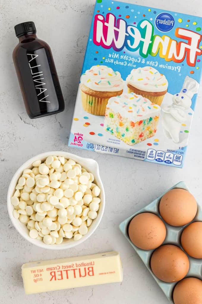 Barrette di biscotti da preparato per torte 16 a box of funfetti cake mix, a bottle of vanilla extract, a bowl of white chocolate chips, a crate of eggs, and a stick of butter