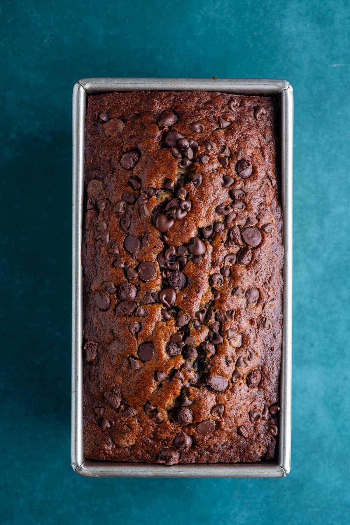 Il Miglior Pan di Banane con Gocce di Cioccolato 17 Pane alle banane e gocce di cioccolato che cuoce in uno stampo da plumcake su una superficie color ottanio scuro.