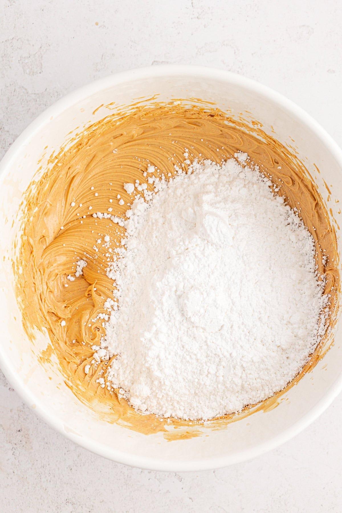 Una ciotola bianca contenente un impasto cremoso di burro d'arachidi con un mucchio di zucchero a velo sopra, pronto per essere mischiato.
