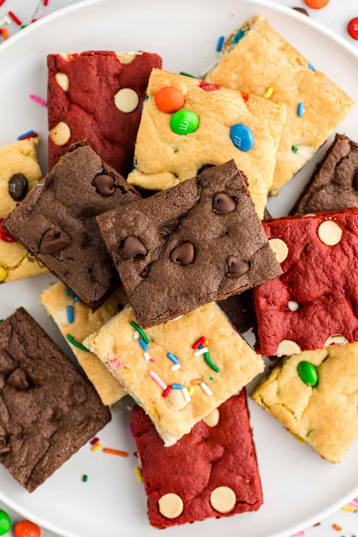 Barrette di biscotti da preparato per torte 17 an assortment of cake mix cookie bars piled on top of each other including m&M, chocolate, red velvet, and funfetti