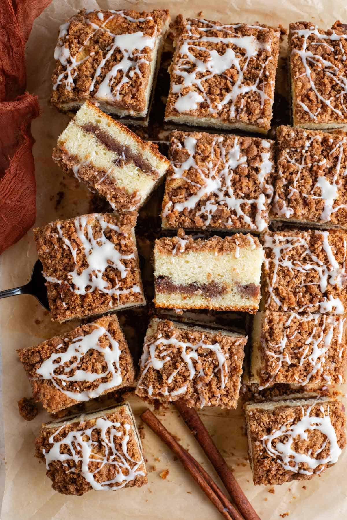 Ricetta Torta Umida al Caffè 3 Fette di torta al caffè disposte su carta marrone, alcune di lato, una forchetta, un asciugamano arancione e bastoncini di cannella