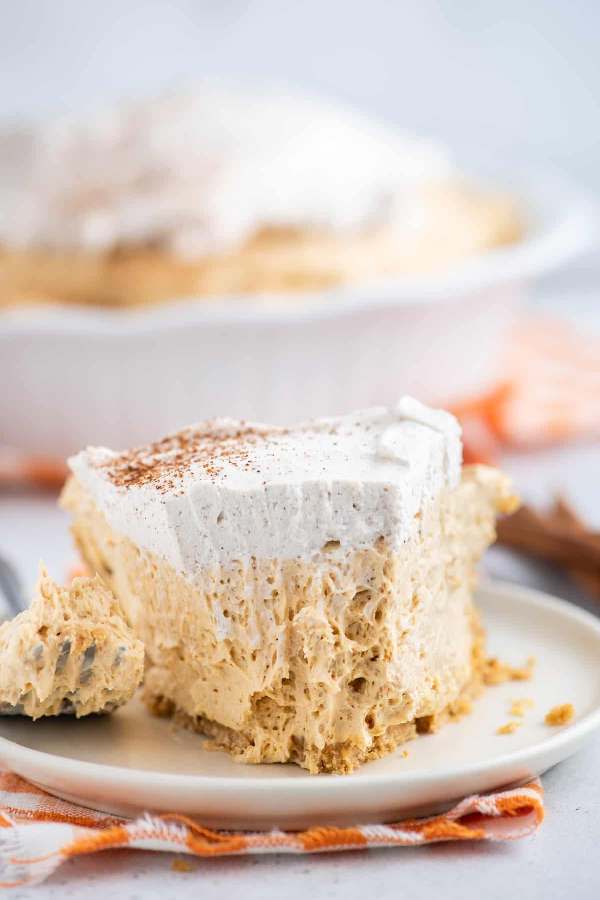Questa torta di zucca senza cottura, veloce e facile, è leggera e cremosa - una deliziosa variante della classica torta di zucca. Una forchetta taglia una fetta di torta di zucca senza cottura.