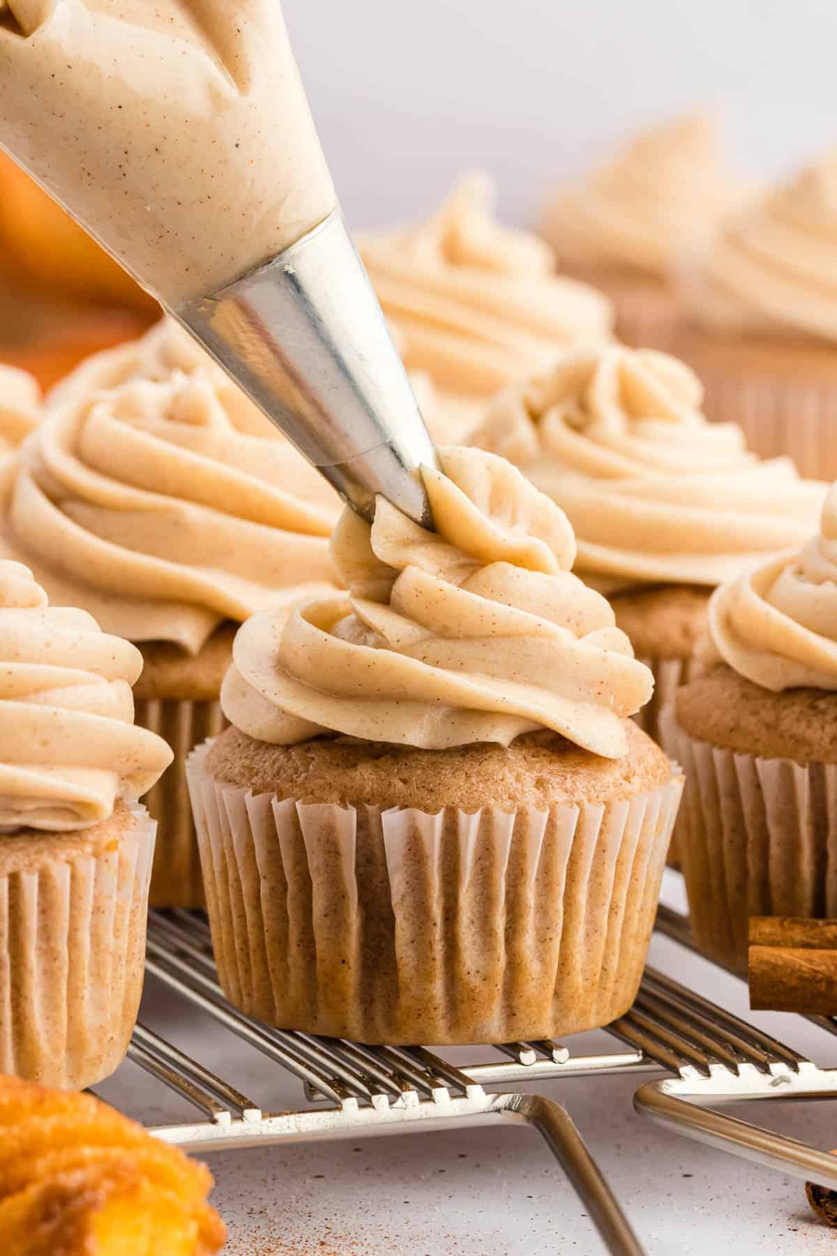 **Glassa al formaggio cremoso alla cannella** 3 Glaseado de queso crema con canela vertiéndose sobre un cupcake en una rejilla de enfriamiento con más cupcakes ya glaseados