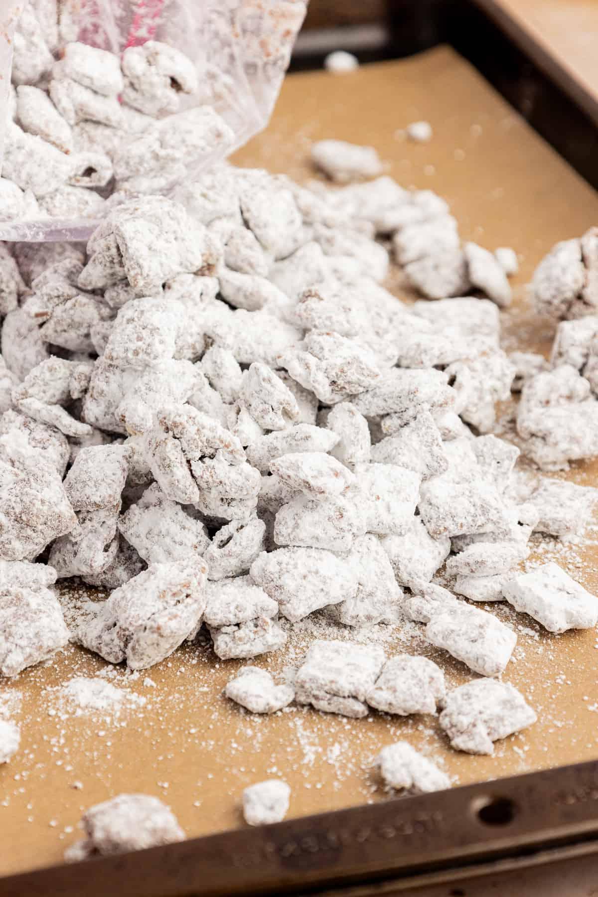 Un mucchio di puppy chow rovesciato da una busta con chiusura a zip su una teglia foderata con carta da forno