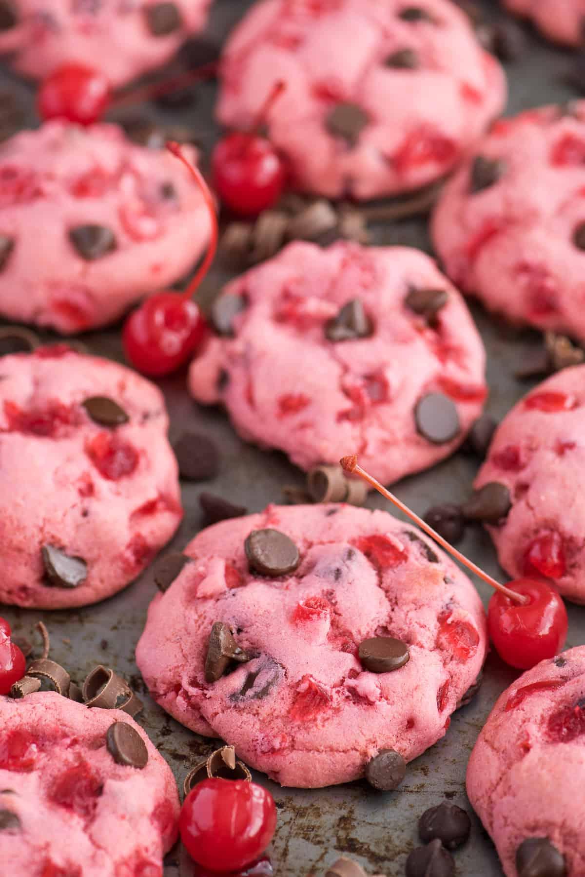 Ricetta di biscotti alle ciliegie maraschino spessi e masticabili! Ricetta di biscotti alle ciliegie candite. biscotti rosa alle ciliegie maraschino e gocce di cioccolato su teglia con ciliegie e gocce di cioccolato