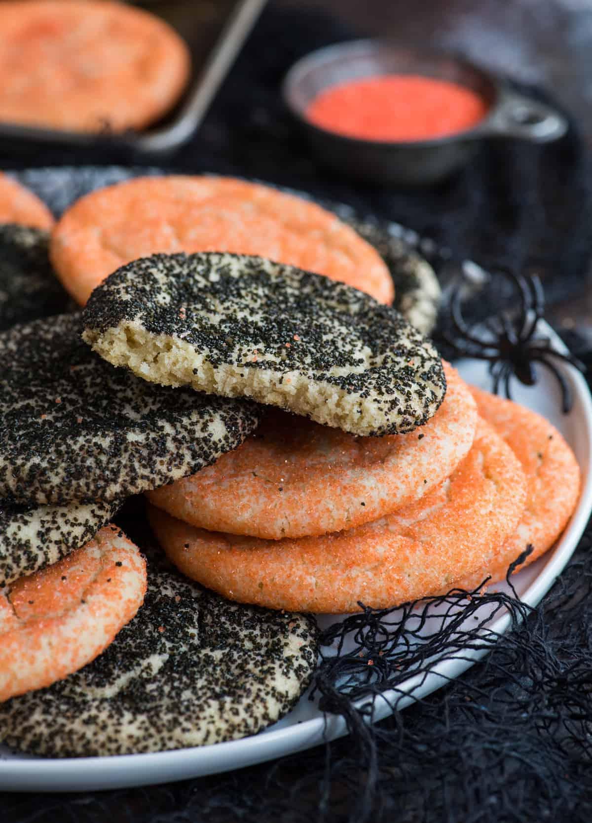 Semplici Biscotti di Zucchero di Halloween 3 Biscotti di zucchero arancioni e neri ammucchiati su piatto bianco con tessuto nero su sfondo nero