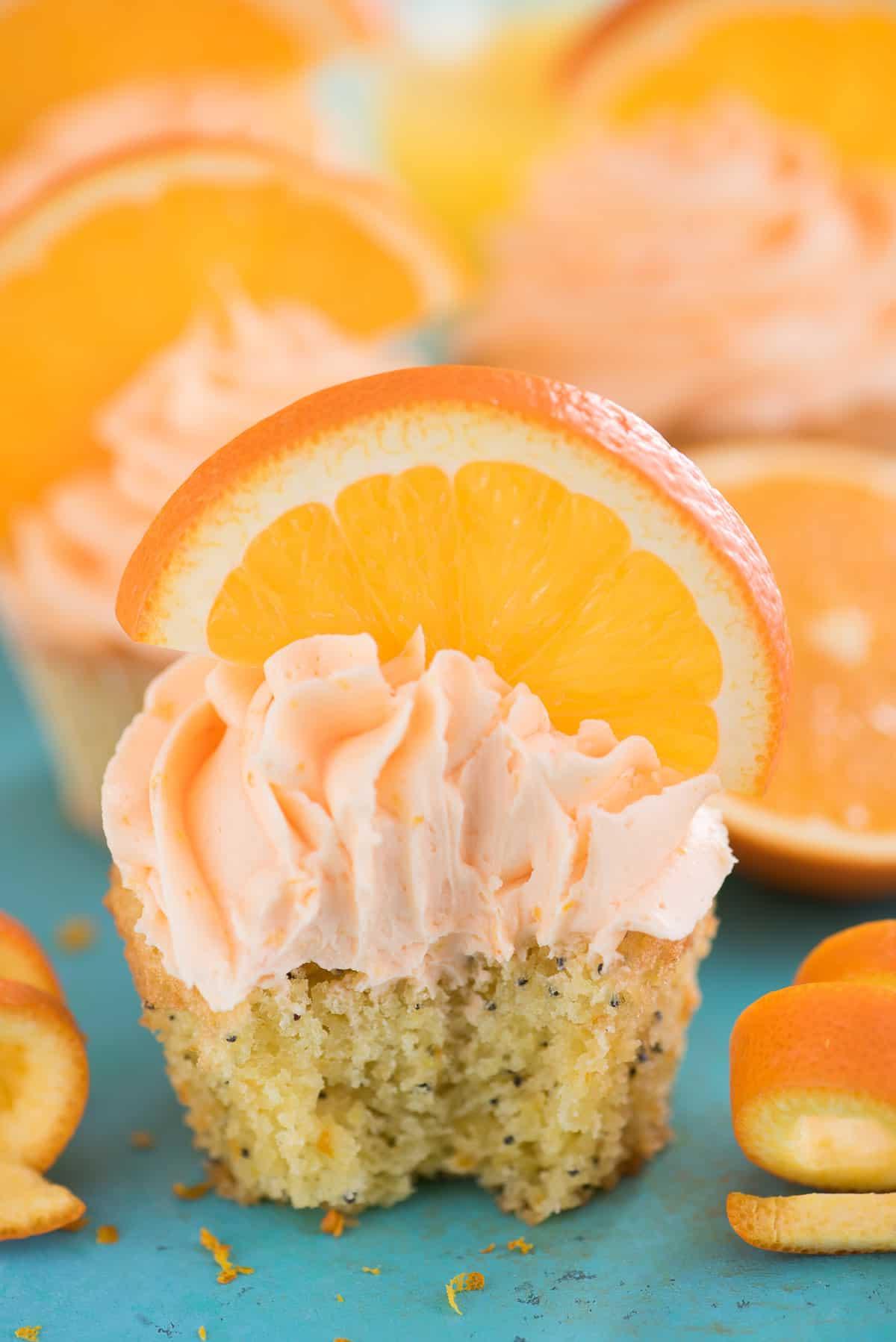 I Cupcake all'Arancia e Semi di Papavero sono una ricetta unica di cupcake agrumati, realizzati con vero succo e scorza d'arancia! Cupcake all'Arancia e Semi di Papavero con fetta d'arancia su sfondo blu