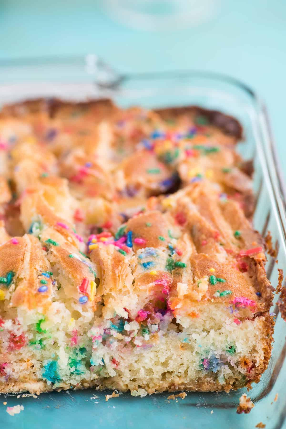 Questa torta terremoto funfetti è un mix per torta bianca arricchito con zuccherini e gocce di cioccolato funfetti. Lo strato di glassa al formaggio cremoso si fonde nella torta creando crepe e fessure in superficie. #earthquakecake #funfetticake #cake Torta terremoto funfetti in teglia di vetro 9x13 pollici