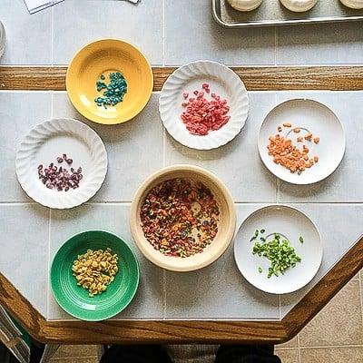 Ciambelle Arcobaleno - queste divertenti ciambelle sono fatte con cereali colorati, cioccolato bianco e cocco grattugiato! Non potrai fare a meno di queste deliziose ciambelle! Separare i cereali Fruity Pebbles in colori diversi, un processo meticoloso.