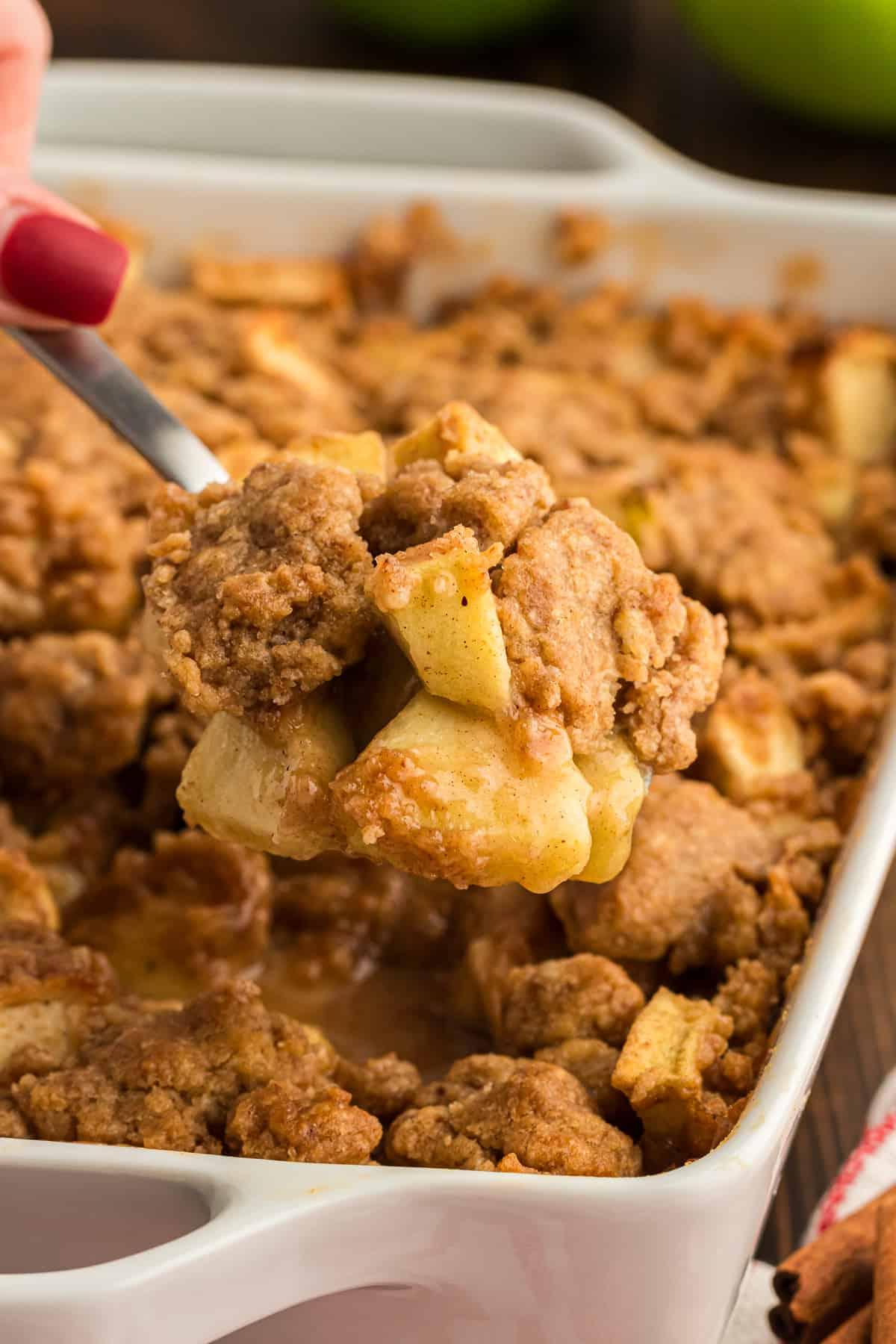 Ricetta Facile di Crumble alle Mele 3 Una pirofila bianca piena di crumble di mele con un cucchiaio di crumble di mele sollevato sopra di essa