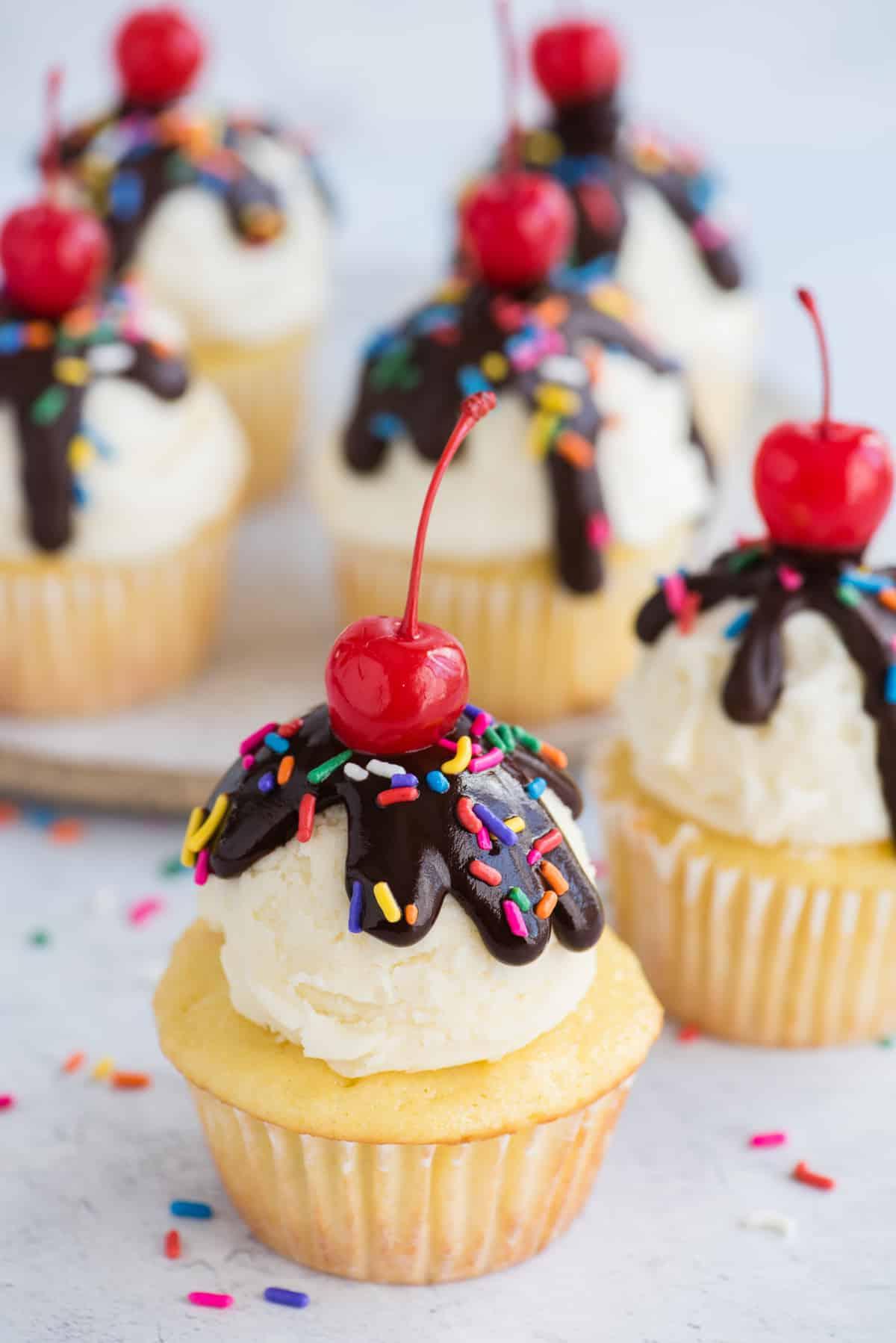 birthday cupcake with scoop of vanilla frosting, chocolate ganache drizzle, sprinkles and maraschino cherry on white background